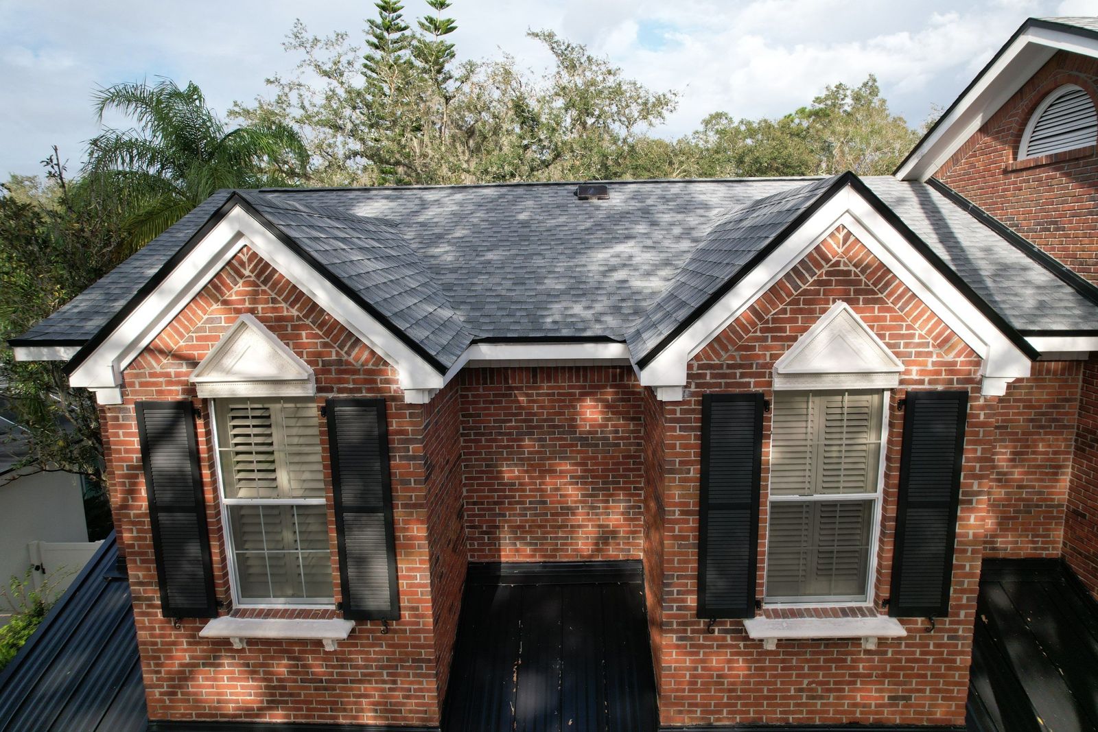 Brick home with new shingle roof and black standing seam low roofs in Tampa