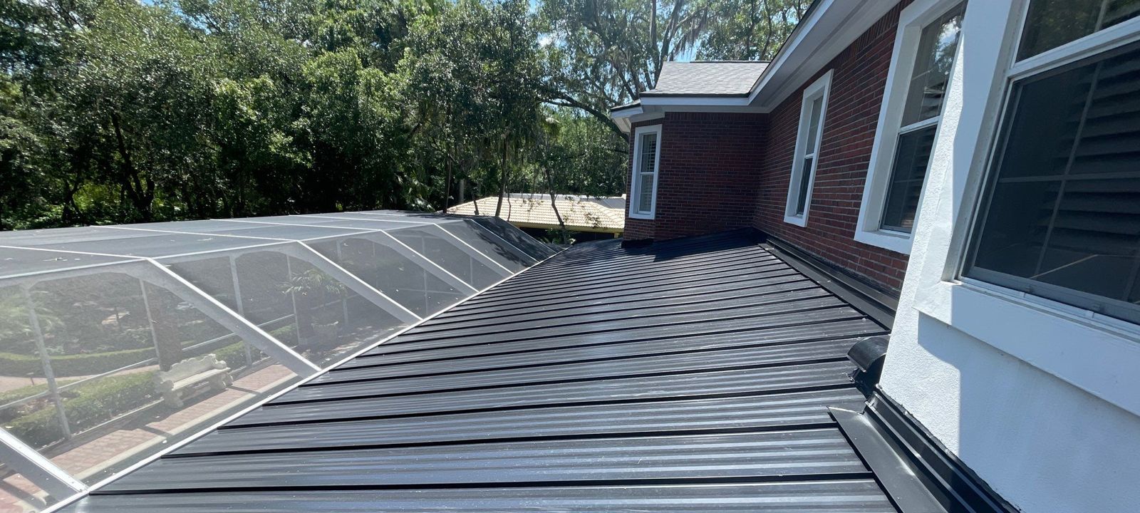 Black standing seam metal patio roof beside a pool enclosure in Tampa FL